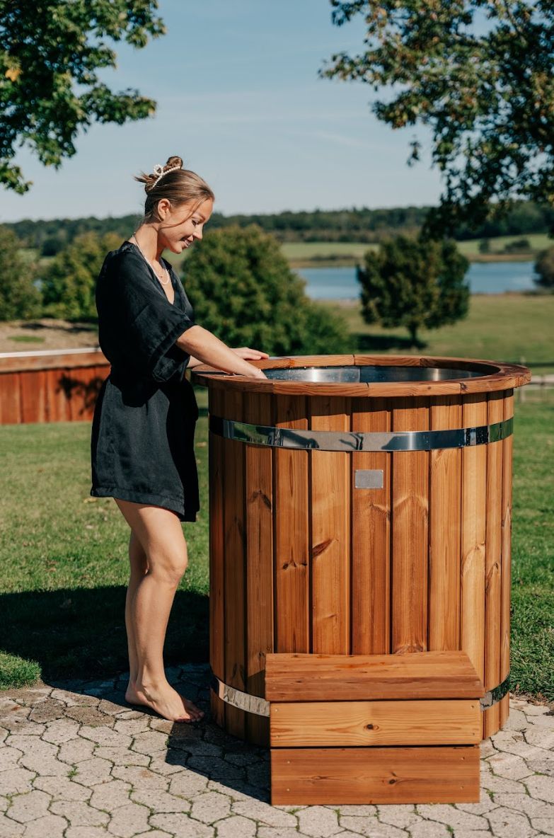 Knyttet kvinde ved iceKore træisbad med udsigt til sø og træer.