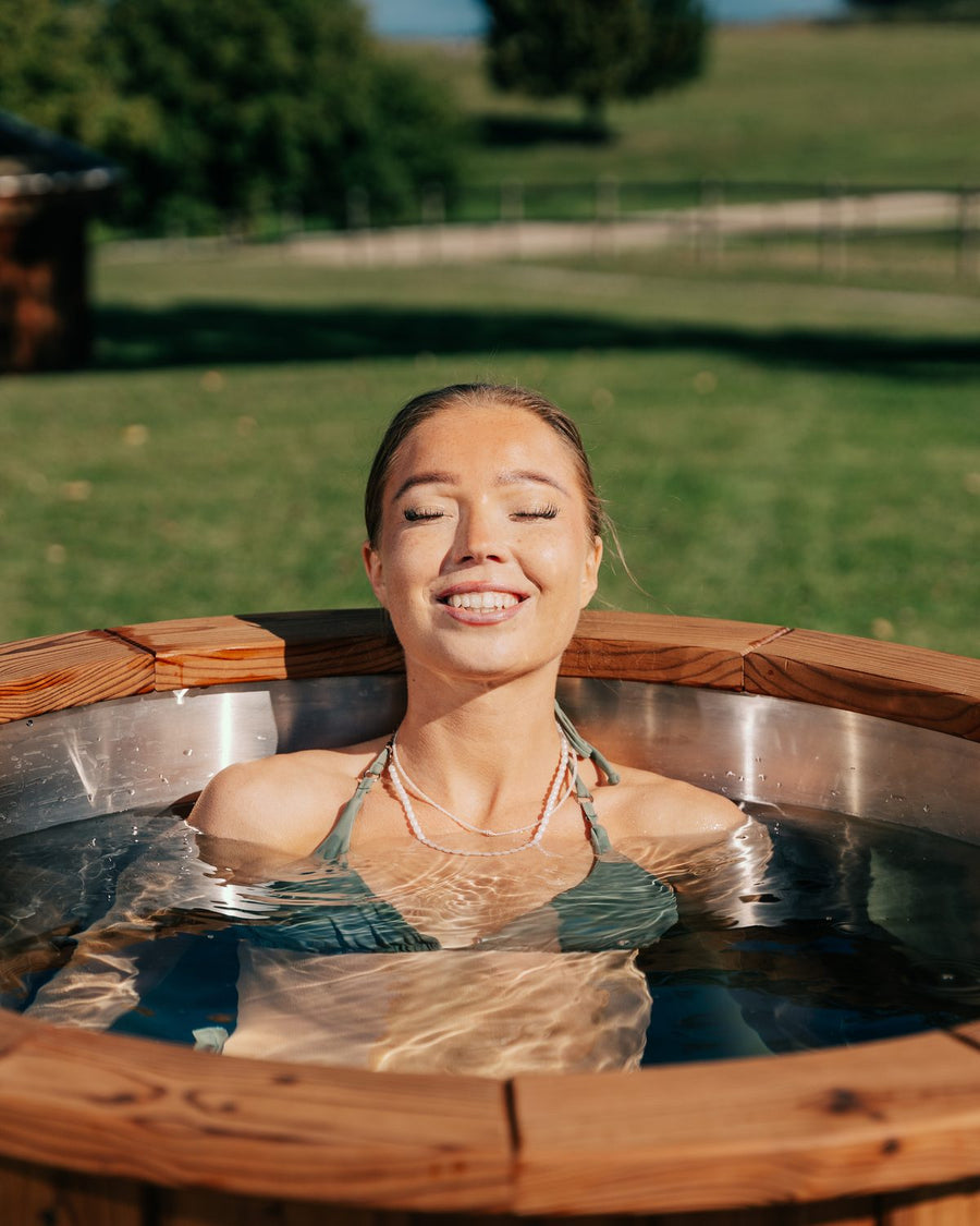 Kvinde smiler med lukkede øjne i et iceKore isbad i thermotræ i haven